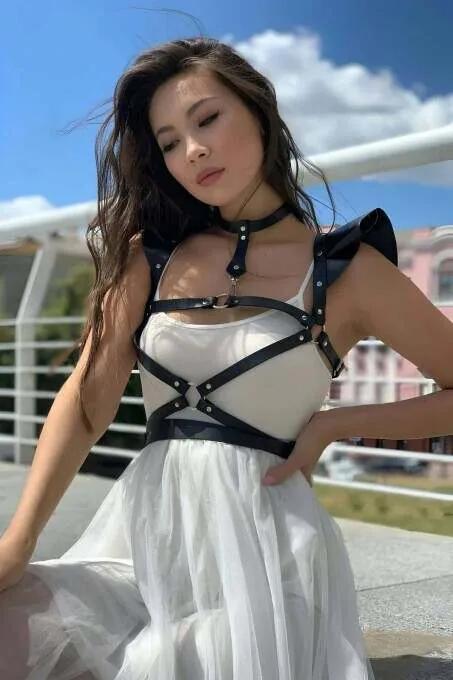 siyah suni deri askılı vücut harness, merkezi O-halka ve yapılandırılmış omuz kapakları, beyaz elbise üzerine giyilmiş